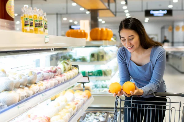 Güzel, genç Asyalı bir kadın alışveriş arabasını itiyor ve süpermarketten portakal alıyor. Alışveriş süpermarketi konsepti.