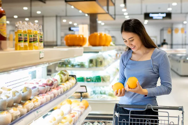 Güzel, genç Asyalı bir kadın alışveriş arabasını itiyor ve süpermarketten portakal alıyor. Alışveriş süpermarketi konsepti.