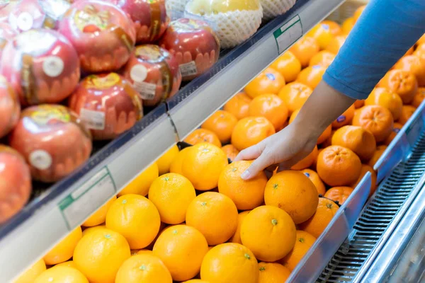 Güzel, genç Asyalı bir kadın alışveriş arabasını itiyor ve süpermarketten portakal alıyor. Alışveriş süpermarketi konsepti.