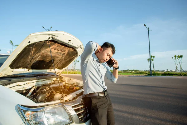 Asian man calling for help by a broken car on road