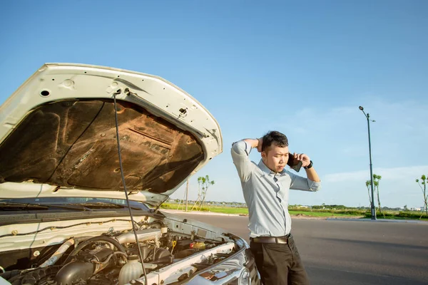 Asian man calling for help by a broken car on road