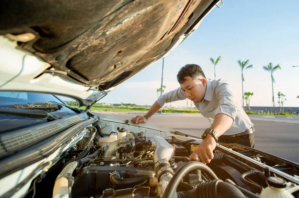 Genç adam bozuk arabasının önünde duruyor ve motoru kontrol etmek için kaputu açıyor.