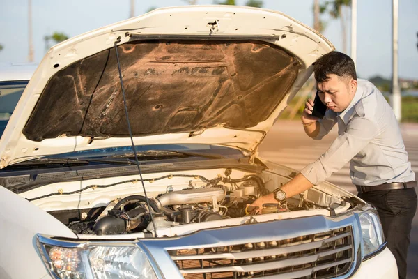 Asian man calling for help by a broken car on road