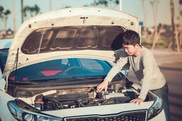 Genç adam bozuk arabasının önünde duruyor ve motoru kontrol etmek için kaputu açıyor.