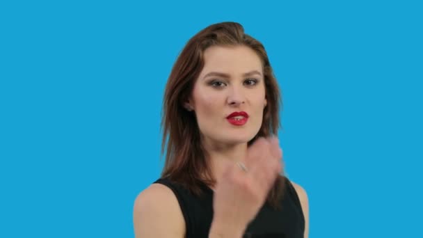 Genç kadın üzerinde mavi arka plan izole bir öpücük üfleme — Stok video