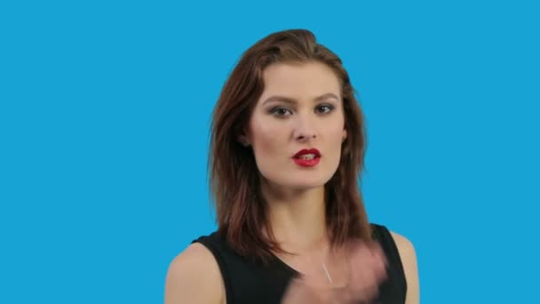 Крупный план молодой женщины, дующей поцелуй изолирован на синем фоне — стоковое видео
