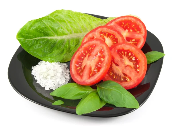 Dilimlenmiş taze domates fesleğen ile yaprakları salata yaprağı ve deniz tuz siyah plaka üzerinde beyaz izole