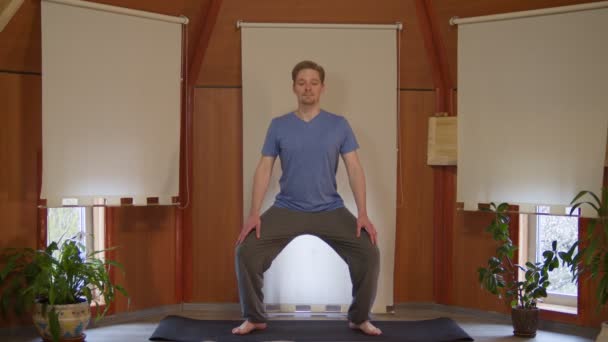 Blanke man in blauw t-shirt en broek oefenen yoga pose op yoga mat en zich richten op getrokken naar voren handen thuis — Stockvideo