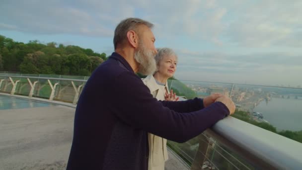 Старый бородатый мужчина и жена разговаривают, любуясь закатом солнца в городе — стоковое видео