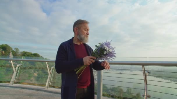 Старший бородатый мужчина с букетом цветов ждет супруга — стоковое видео