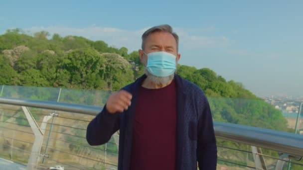 Starší muž odkládá lékařskou masku a zhluboka se nadechuje venku — Stock video