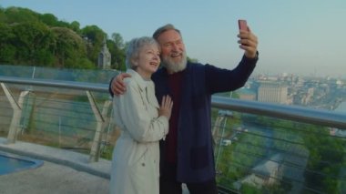 Büyükannem ve büyükbabam terasta dururken gülümseyip selfie çekiyorlar.