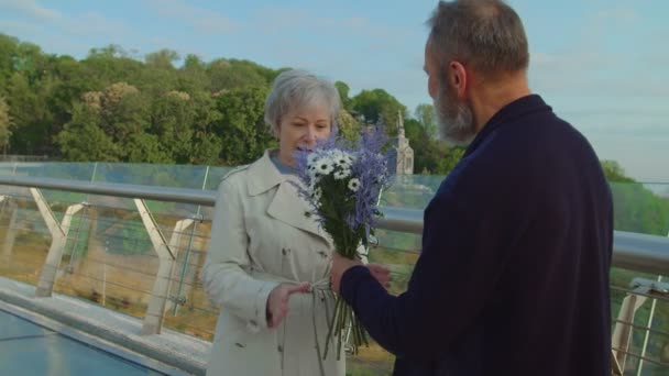 Elderly man holding bouquet behind back and gifting it to senior woman — Stock Video
