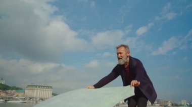 Kıdemli adam nehir ya da göl kıyısında kumlara battaniye koyuyor.