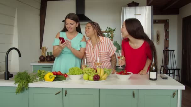 スマートフォンを呼び出す友人とキッチンで踊る混合レースの女性 — ストック動画
