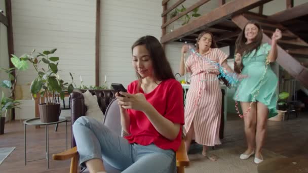 Młoda kobieta przeglądająca smartfona na tle tańczących przyjaciół — Wideo stockowe