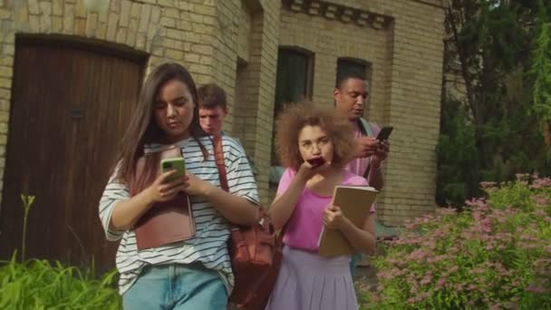 Diverse students obsessed with smartphones outdoors leaving classes — Vídeo de Stock