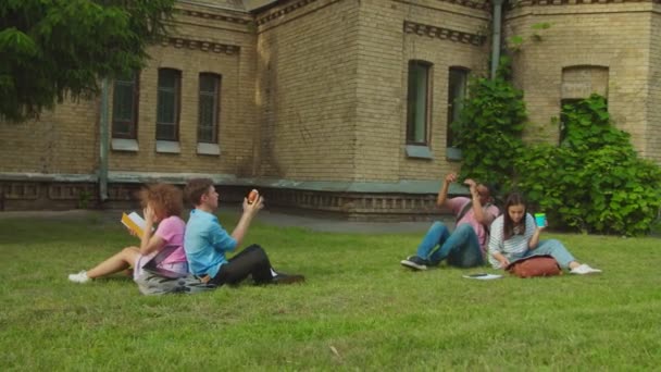 Group of mixed race students having break sitting on lawn outdoors — Stock video