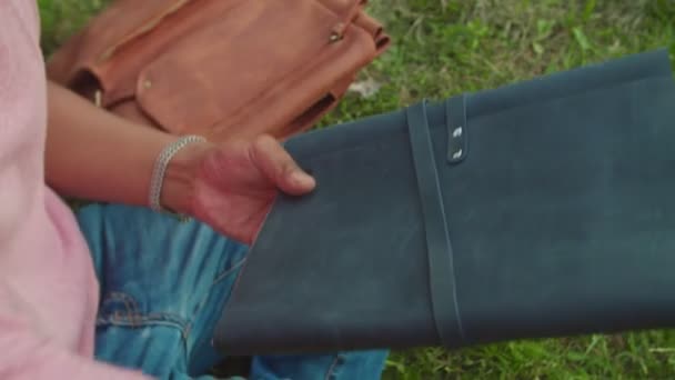 Hombre joven abriendo cuaderno de dibujo de cuero sentado en el césped del campus al aire libre — Vídeo de stock