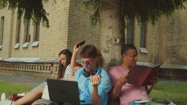 Primo piano degli studenti che studiano utilizzando gadget seduti sotto l'albero all'aperto — Video Stock