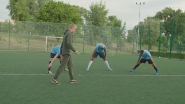 Futbolcular açık havada geniş bacaklı ön bükme egzersizi yapıyorlar.