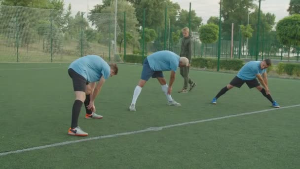 Fotballspillere som strekker seg, utfører fremre bøyeøvelse utendørs – stockvideo