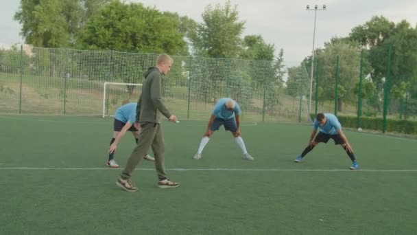 Voetballers met brede benen naar voren buigen oefening buiten — Stockvideo