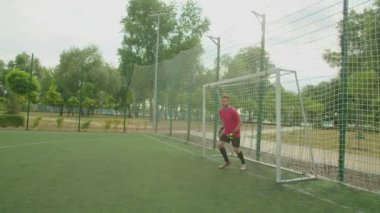 Futbol kalecisi dışarıda penaltı alanından futbol topuna vuruyor.