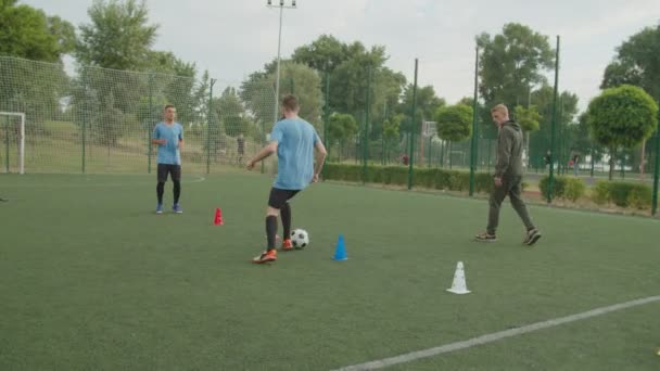 Jogadores de futebol realizando exercícios de driblagem com cones, bola ao ar livre — Vídeo de Stock