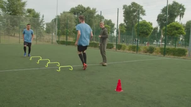 Entrenador de fútbol que controla la realización de ejercicio de barrera de salto al aire libre — Vídeo de stock