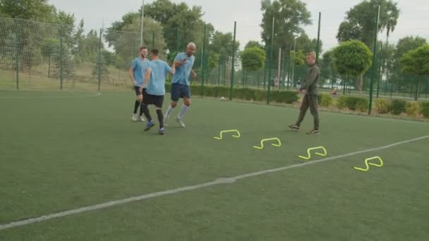 Футболисты выполняют упражнения по прыжкам с барьерами с тренером на открытом воздухе — стоковое видео