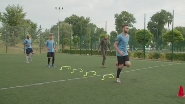 Fotballspillere som vekselvis utfører hoppebarrierer, trener utendørs – stockvideo