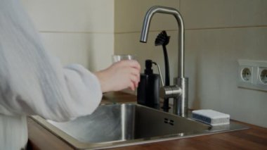 İçerideki musluktan taze filtrelenmiş suyu cama döken kadın.