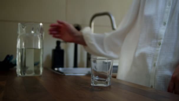 Closeup γυναικεία χέρια ρίχνει νερό σε γυαλί από κανάτα στην κουζίνα — Αρχείο Βίντεο