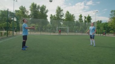 Futbol oyuncuları futbol sahasında antrenman yaparken topu göğsüne takıyorlar.