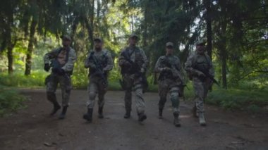 Bir grup asker şafakta tek sıra halinde kameraya doğru yürüyorlar.
