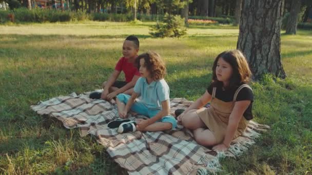 Elever som sitter på rutig mark och lyssnar på skollärare utomhus i gryningen — Stockvideo