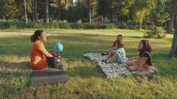 Colegiala enseñando geografía lección a los alumnos de raza mixta al aire libre — Vídeo de stock