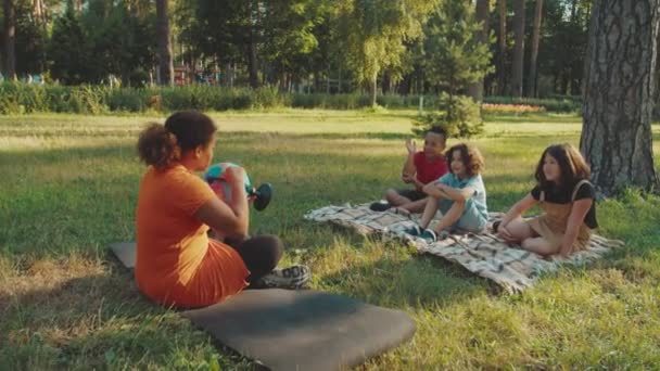 Profesor de escuela usando globo, haciendo preguntas a los niños al aire libre — Vídeo de stock