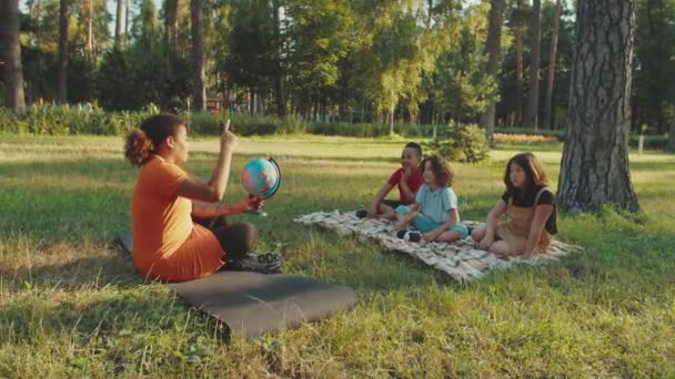 Schoolleraar wijzend op wereldbol, vragen stellen aan leerlingen buiten — Stockvideo