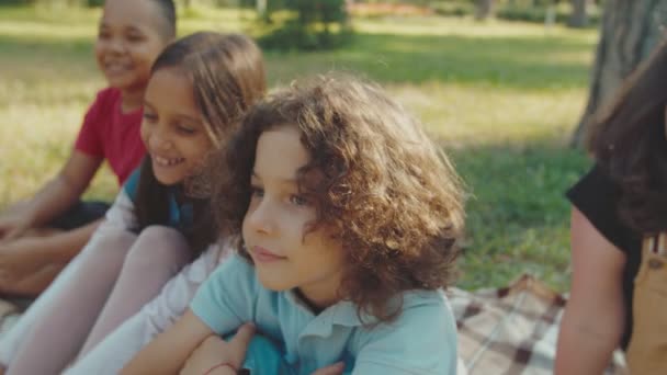 Vielfältige Kinder lachen, sitzen auf karierten Draußen — Stockvideo