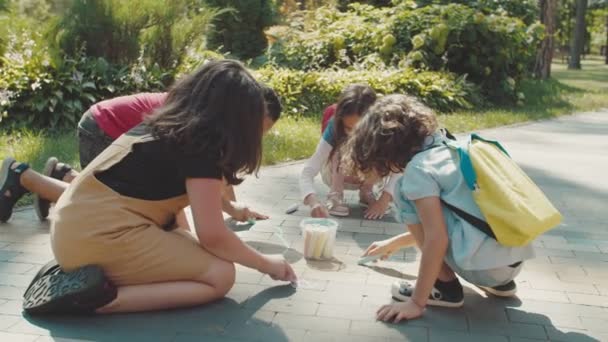 Vielfältige Kinder malen mit Buntstiften auf Bürgersteig im Freien — Stockvideo