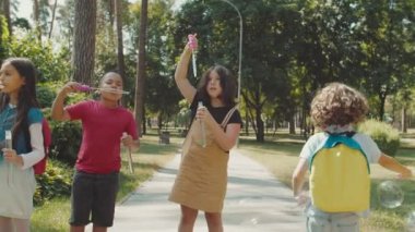 Çoklu etnik çeşitlilikteki çocuklar dışarıda baloncuklar çıkarıyorlar.