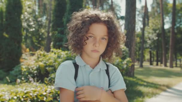 Retrato de menino encaracolado com mochila olhando para a câmera ao ar livre — Vídeo de Stock