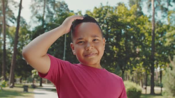 Porträtt av söt pojke tittar in i kameran, ler charmigt utomhus — Stockvideo