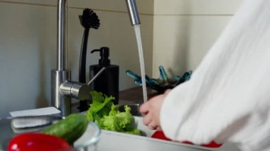 Mutfak lavabosunda domates yıkayan tanınmayan bir kadın.