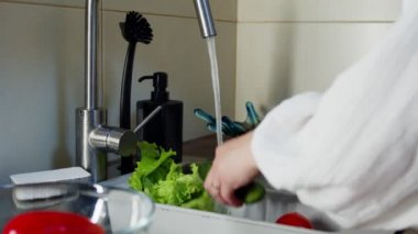 Mutfak lavabosunda salatalık yıkayan tanınmayan bir kadın.