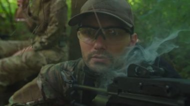 Makineli tüfekli bir portre askeri sigara içiyor, askerleri koruyor.