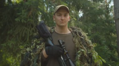 Açık havada keskin nişancı tüfeğiyle ghillie kıyafetli genç bir askerin portresi.