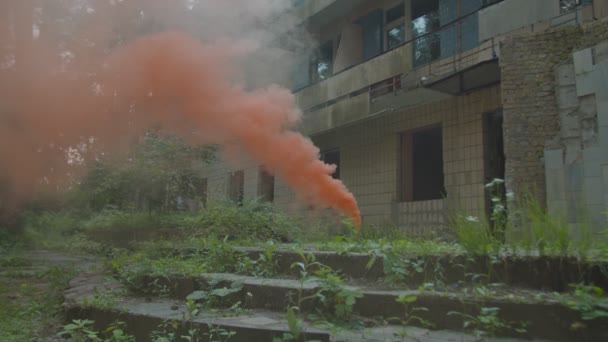 Χειροκίνητη φωτοβολίδα που εκπέμπει πορτοκαλί καπνό με εγκαταλελειμμένο κτίριο στο παρασκήνιο — Αρχείο Βίντεο